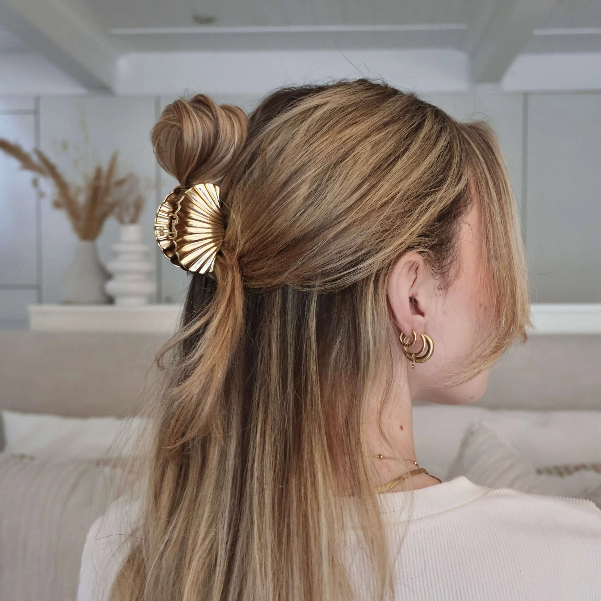 Woman wearing a gold statement shell hair clip with soft waves in a neutral setting