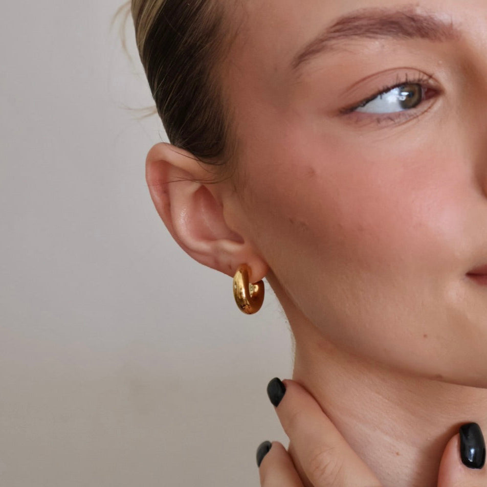 Close-up of a woman wearing gold hoop earrings and rings on a neutral background