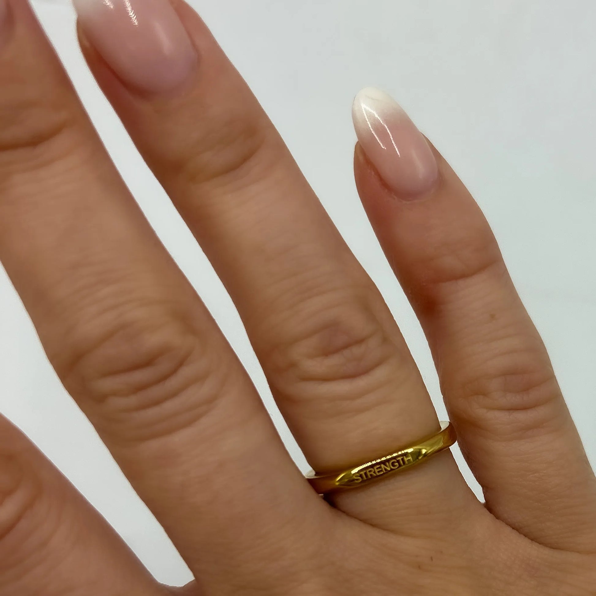 A close-up image of a person's finger wearing a gold-plated ring with the word 'AFFIRMATION' engraved on it.