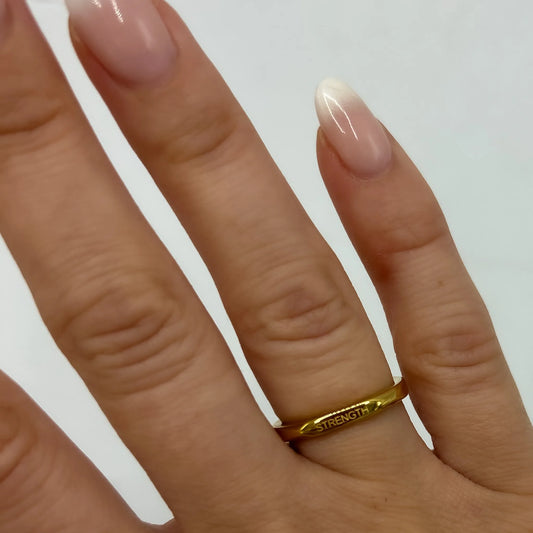 A close-up image of a person's finger wearing a gold-plated ring with the word 'AFFIRMATION' engraved on it.