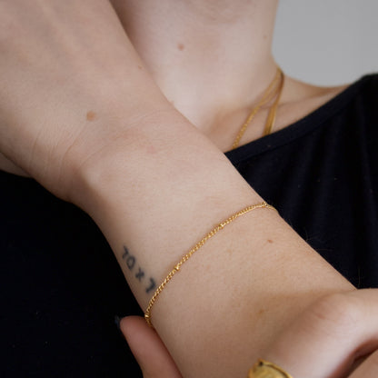 Close-up of a person's wrist with gold bracelet with tiny gold beads on a neutral background